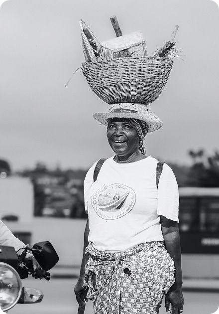A smiling woman in a black and white photo, balancing a large woven basket on her head.